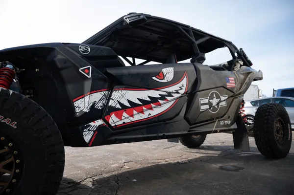 A Can-Am Maverick X3 Max side-by-side with a black, tan, and red tiger shark plane custom vinyl wrap.