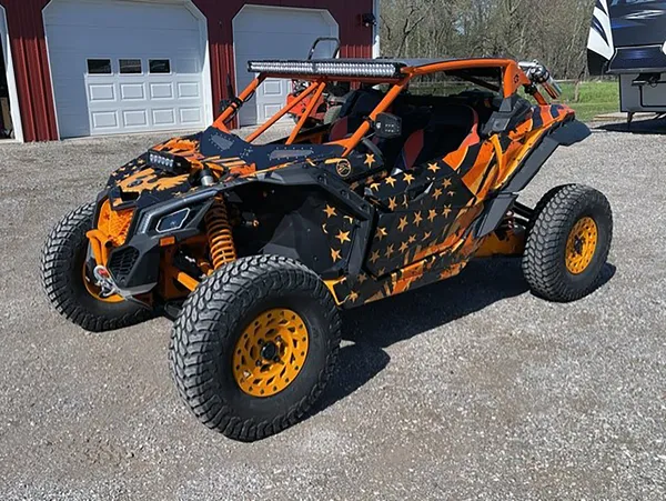 A Can-Am Maverick X3 side-by-side with a orange and  black grunge American Flag custom vinyl wrap.