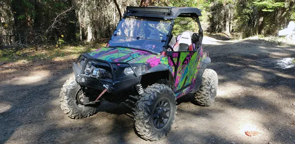 A Polaris RZR 2 Door side-by-side with a teal, green and pink Bombsquad custom vinyl wrap.