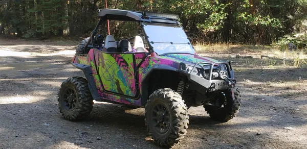 A Polaris RZR 2 Door side-by-side with a teal, green and pink Bombsquad custom vinyl wrap.