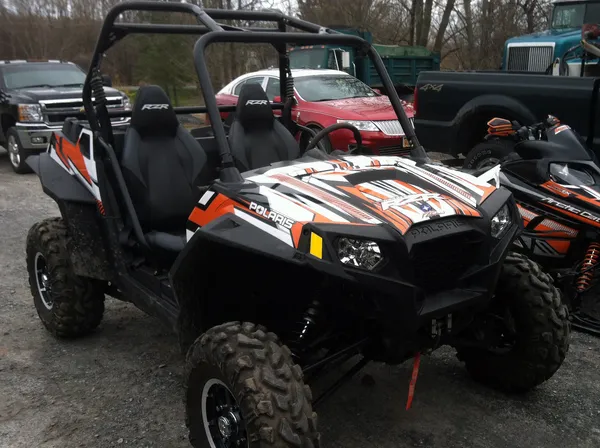 A Polaris RZR 2 Door side-by-side with a blue, black, and orange Bred2Win custom vinyl wrap.