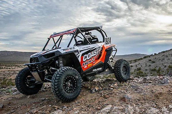 A Polaris RZR XP 2 Door side-by-side with a orange, white, and black Holz Racing custom vinyl wrap.