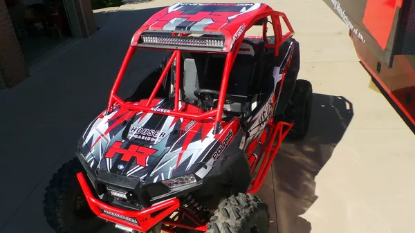 A Polaris RZR XP 2 Door side-by-side with a red, white, and black Houser Racing custom vinyl wrap.