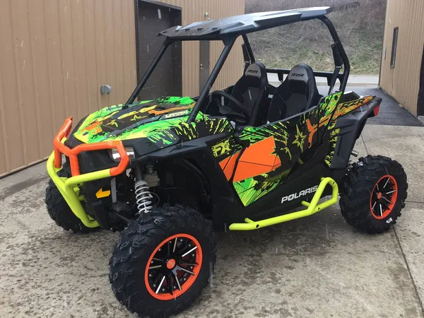 A Polaris RZR XP 2 Door side-by-side with a orange, lime, and black grunge Retrobution custom vinyl wrap.
