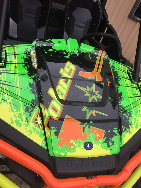 A Polaris RZR XP 2 Door side-by-side with a orange, lime, and black grunge Retrobution custom vinyl wrap.