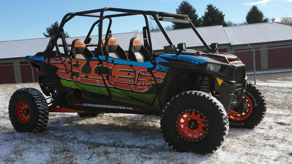 A Polaris RZR XP 4 Door side-by-side with a black, blue, green, and orange grunge Ace Engineering custom vinyl wrap.