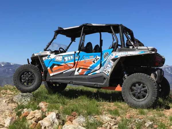 A Polaris RZR XP 4 Door side-by-side with a white, orange, and blue stripes Curtis Mountain King custom vinyl wrap.