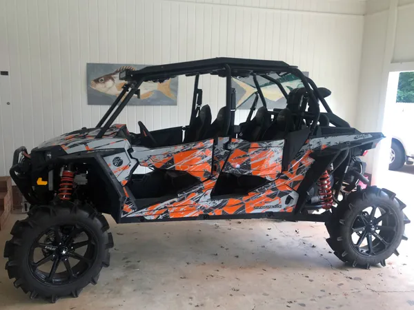 A Polaris RZR XP 4 Door side-by-side with a black, gray, and orange grunge Ruin custom vinyl wrap.