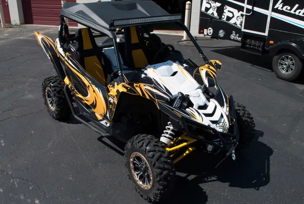 A Yamaha YXZ1000R side-by-side with a yellow, black, and white grunge swirl Surge custom vinyl wrap.