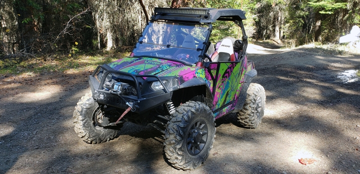A Polaris RZR 2 Door side-by-side with a teal, green and pink Bombsquad custom vinyl wrap.