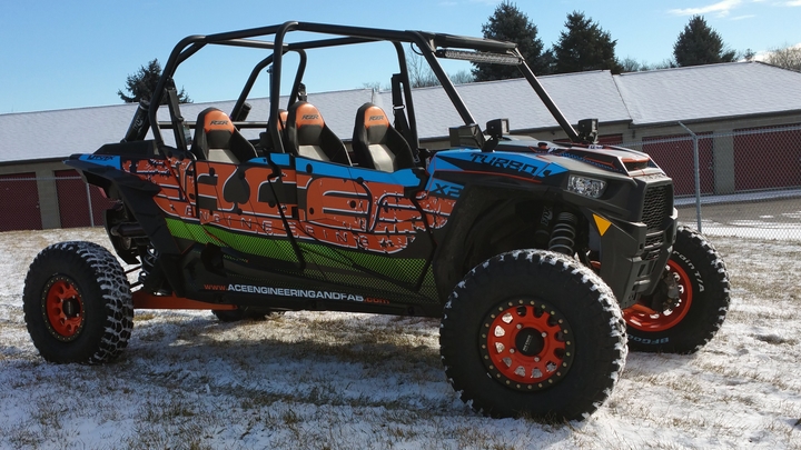 A Polaris RZR XP 4 Door side-by-side with a black, blue, green, and orange grunge Ace Engineering custom vinyl wrap.